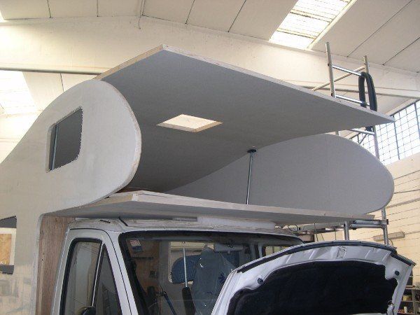 Copertura grigia per camper montata su un camion bianco all'interno di un garage, con un'ampia struttura del tetto sovrastante.