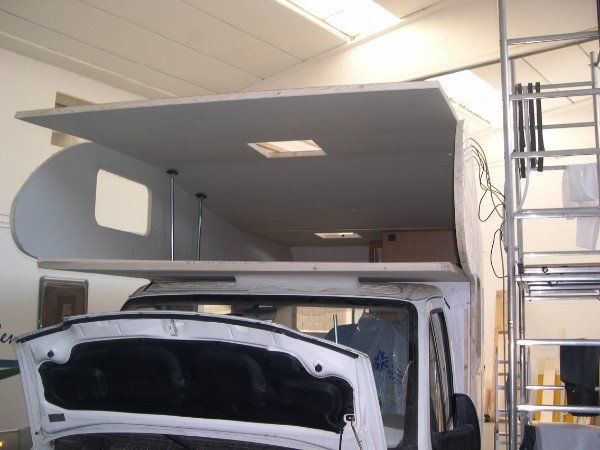 Cabina di un camion grigio in un garage con il cofano anteriore aperto, che lascia intravedere il vano motore e il pannello del tetto sollevato.