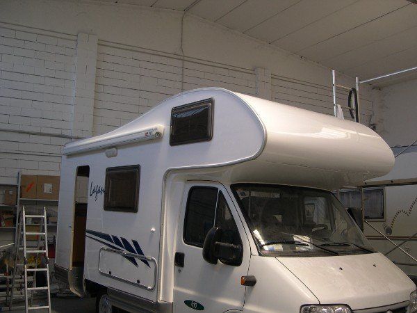Camper bianco parcheggiato all'interno di un garage o di un'officina, con strisce blu scuro e una zona notte rialzata.