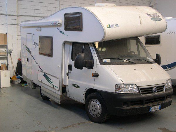 Camper bianco parcheggiato all'interno di un garage, vista frontale angolata.