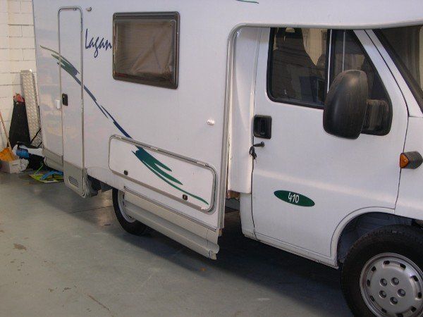 Un camper bianco parcheggiato all'interno di un edificio, con la porta laterale aperta e il finestrino visibile.