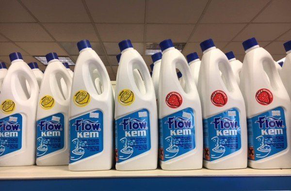 Diverse bottiglie di detersivo Flow Kem di colore bianco con etichette blu e rosse su uno scaffale del negozio.
