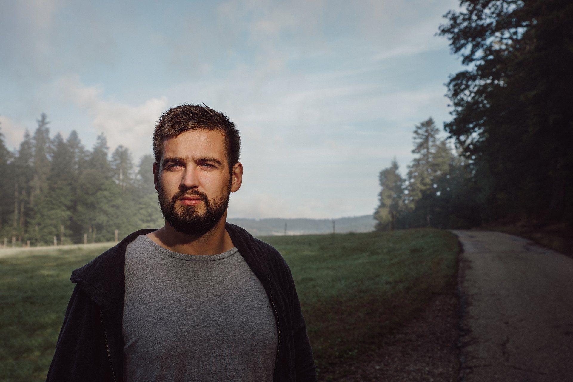 A man with a beard is standing on a dirt road.