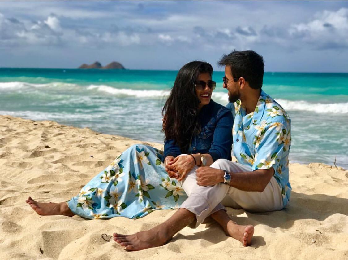 A man and a woman are sitting on the beach looking at each other.