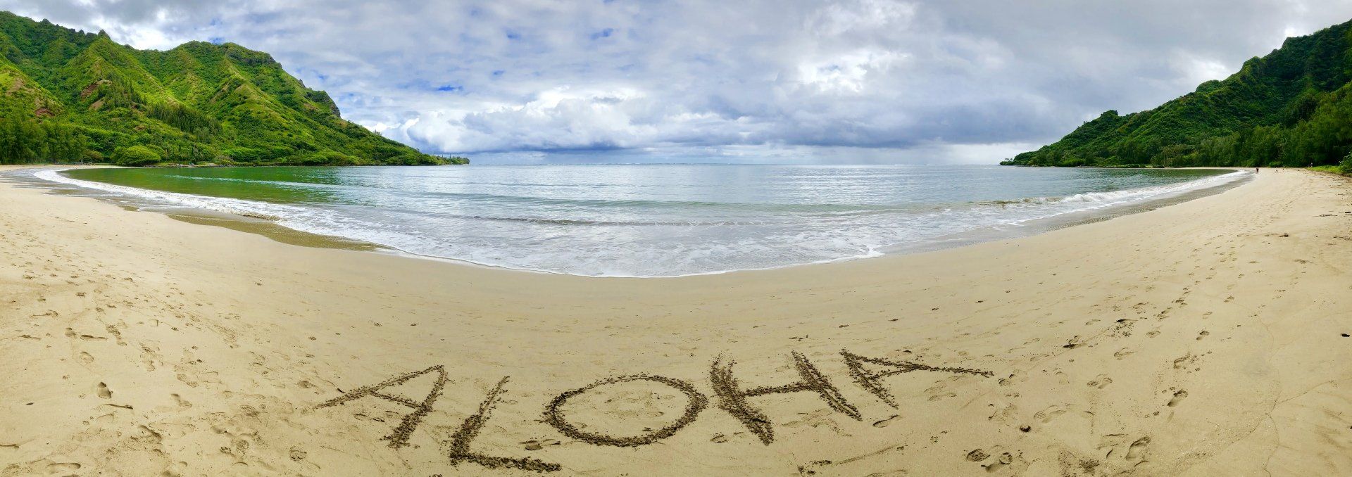 The word aloha is written in the sand on a beach