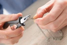 A person is holding a pair of pliers over a chain.