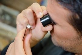 A man is looking at a diamond through a magnifying glass.