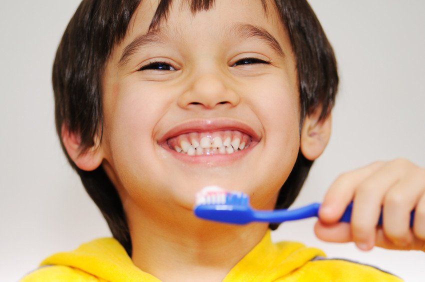 A young boy brushes his teeth and shows his smile