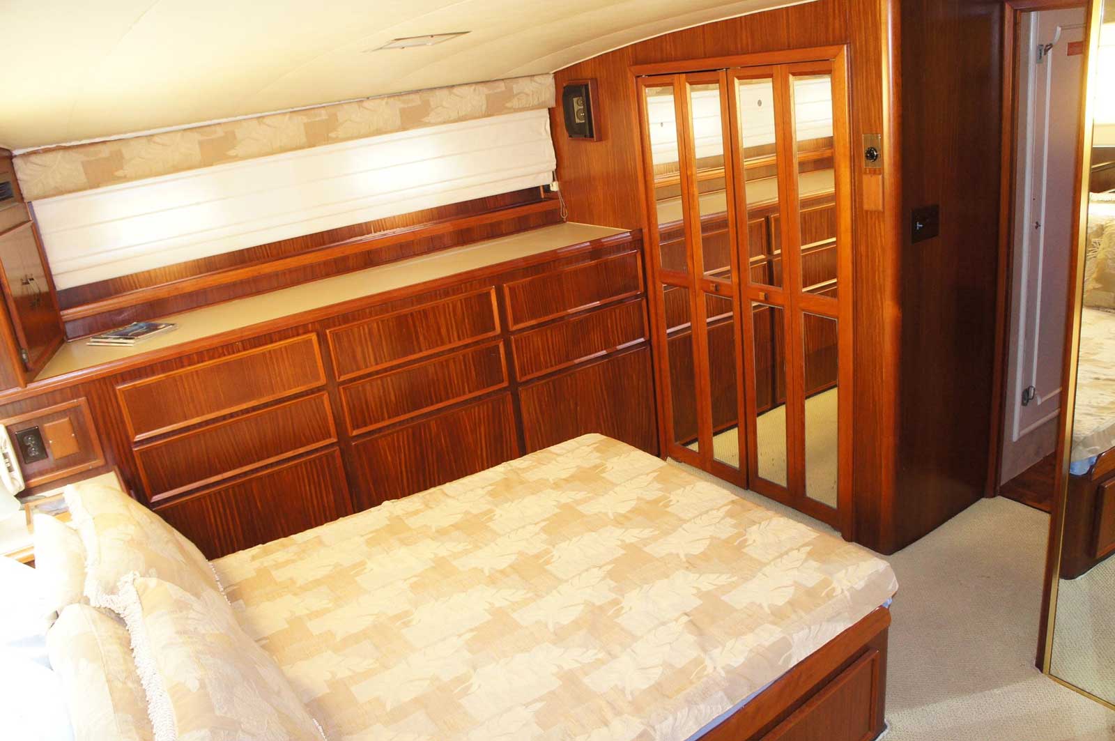 A bedroom on a boat with a bed and dressers.