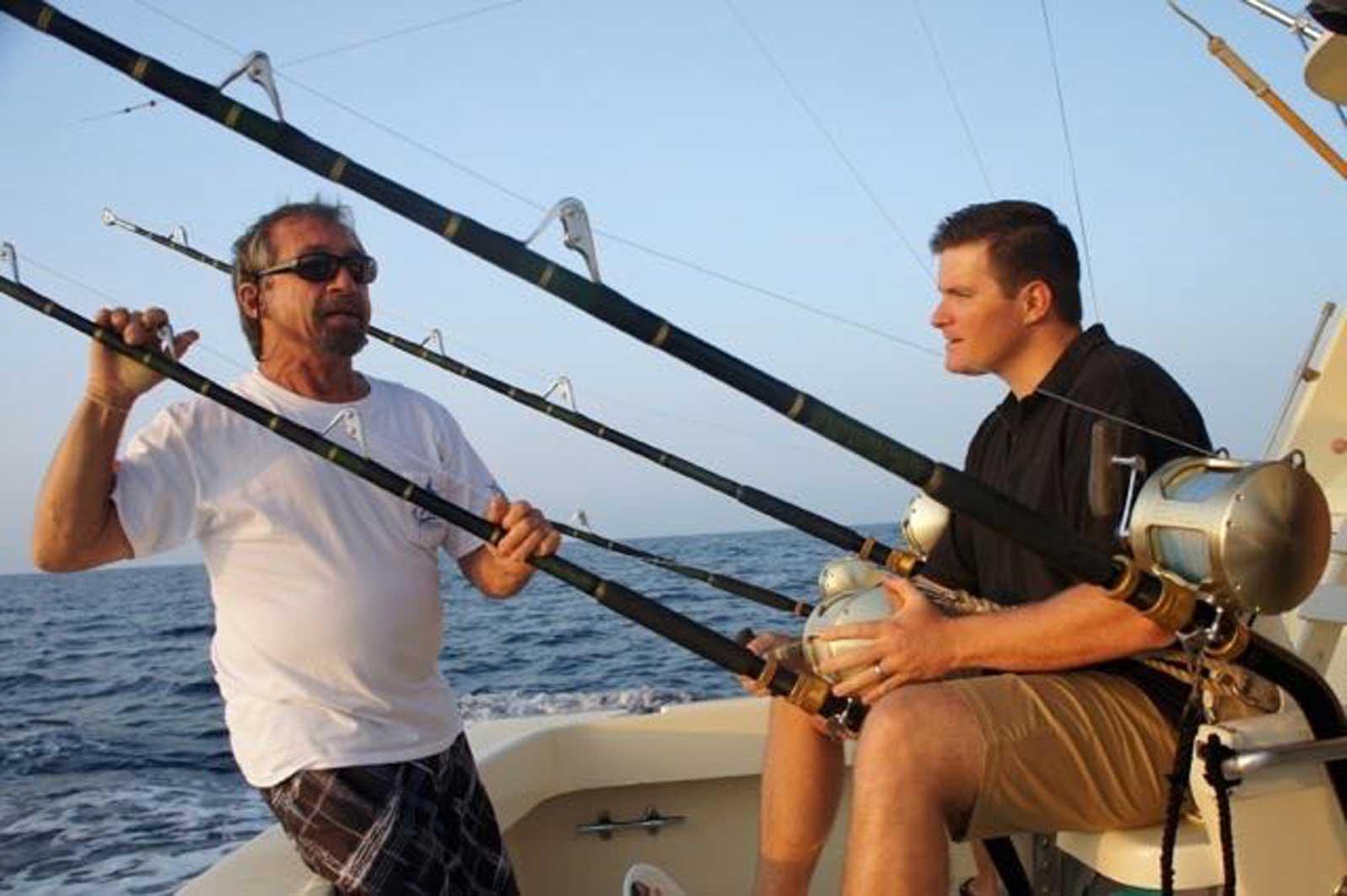 Two men are sitting on a boat holding fishing rods