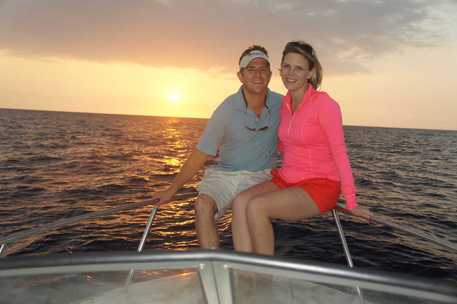 A man and a woman are sitting on a boat in the ocean at sunset.