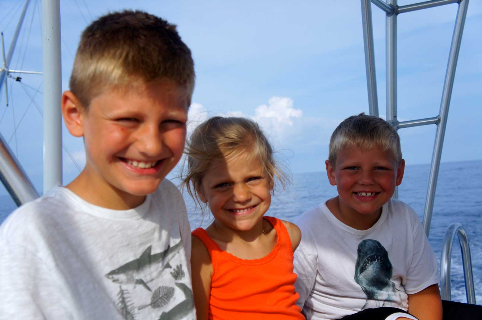Two boys and a girl are posing for a picture on a boat