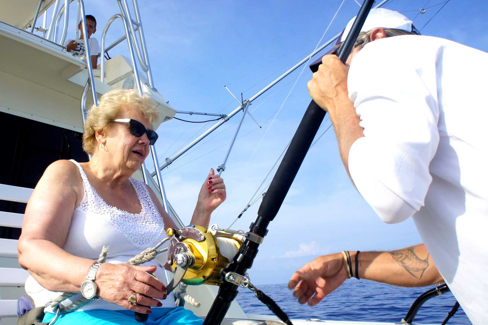 An elderly woman is fishing with a man on a boat