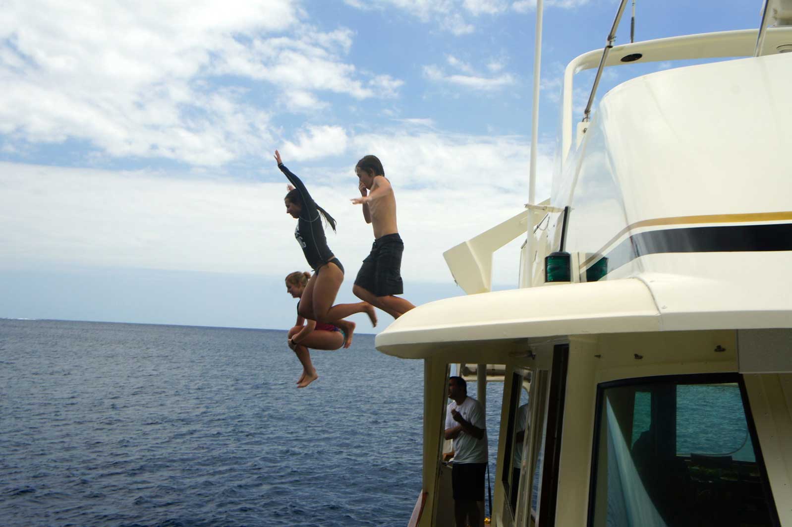 Two people are jumping off a boat into the ocean