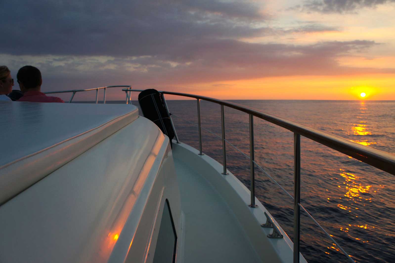 A couple sitting on a boat watching the sunset over the ocean