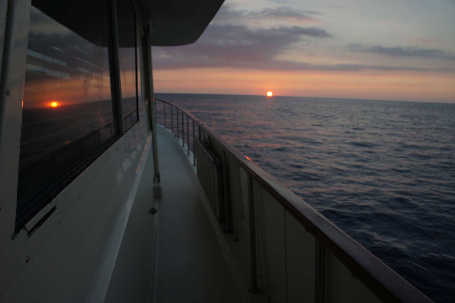 The sun is setting over the ocean from a boat