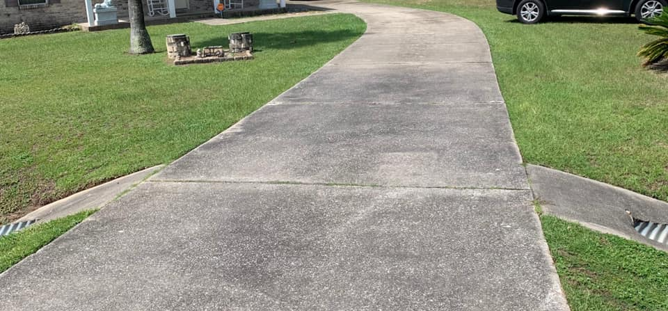 A concrete walkway leading to a house with a car parked on the side of it.