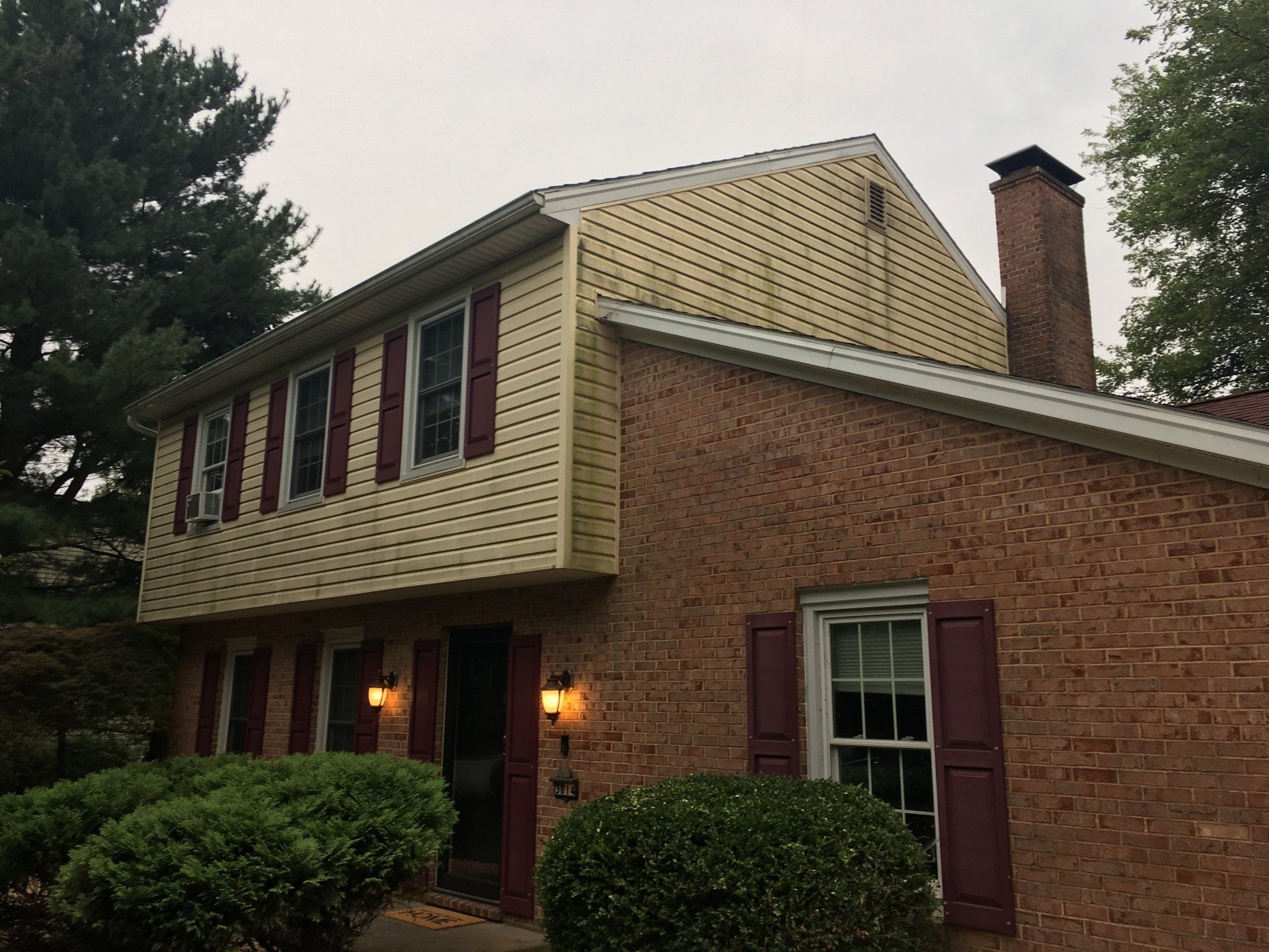 A brick house with a yellow siding and red shutters