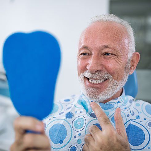 A man is smiling while looking at his teeth in a mirror.