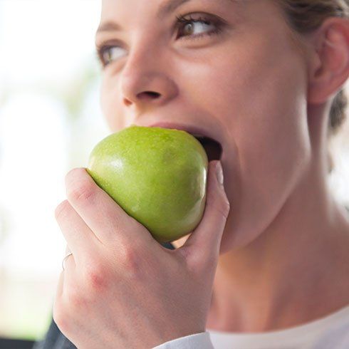A woman is biting into a green apple.