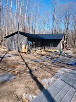 Gray house under construction in a wooded area; blue sky.