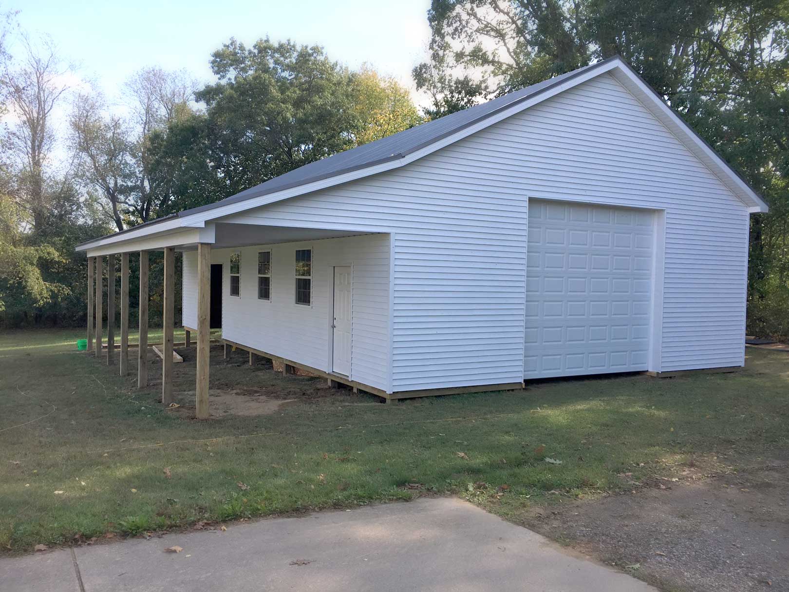 White barn with a covered porch on a grassy lawn with trees in the background.