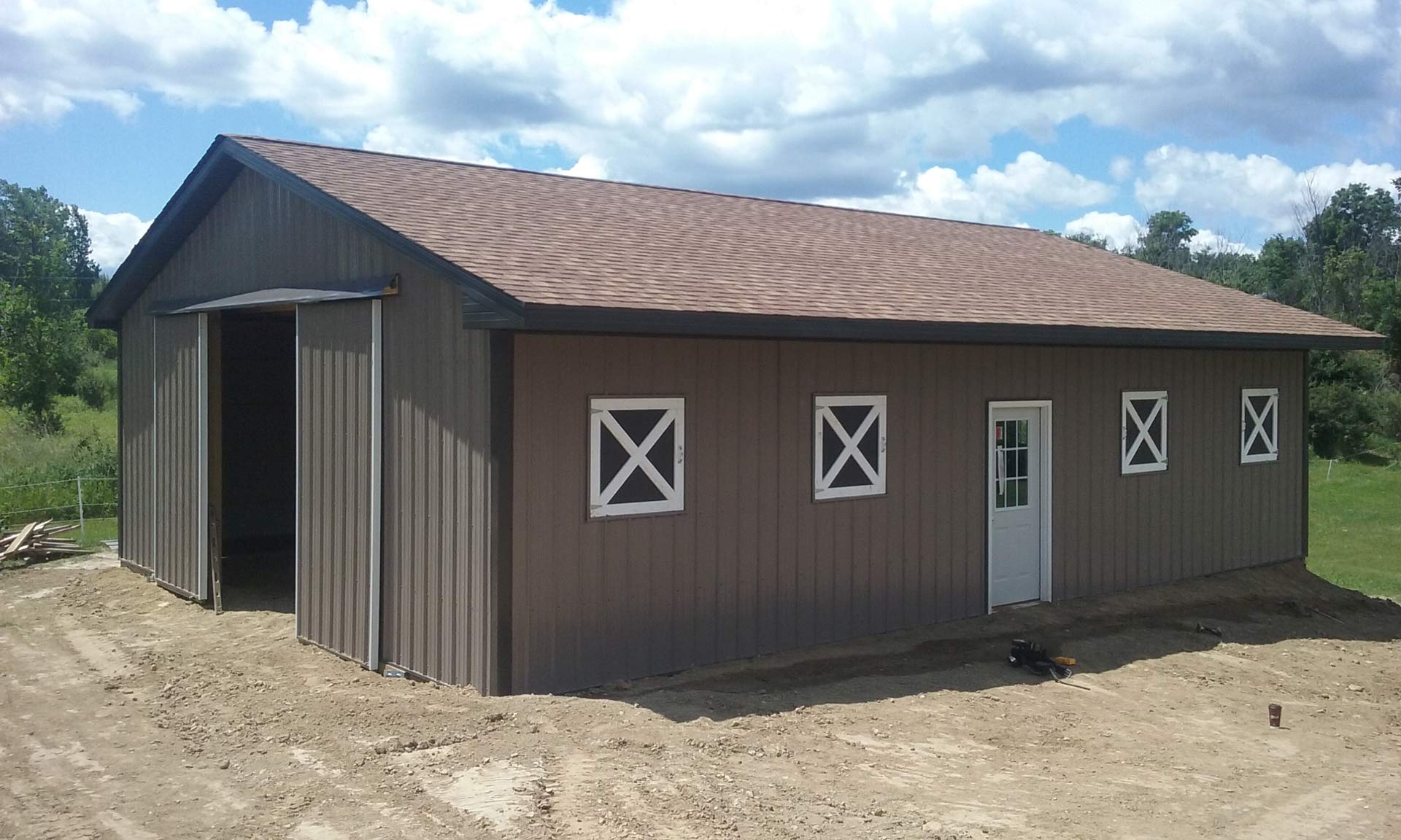Brown metal barn with sliding door and white X-shaped window frames, under a blue sky.