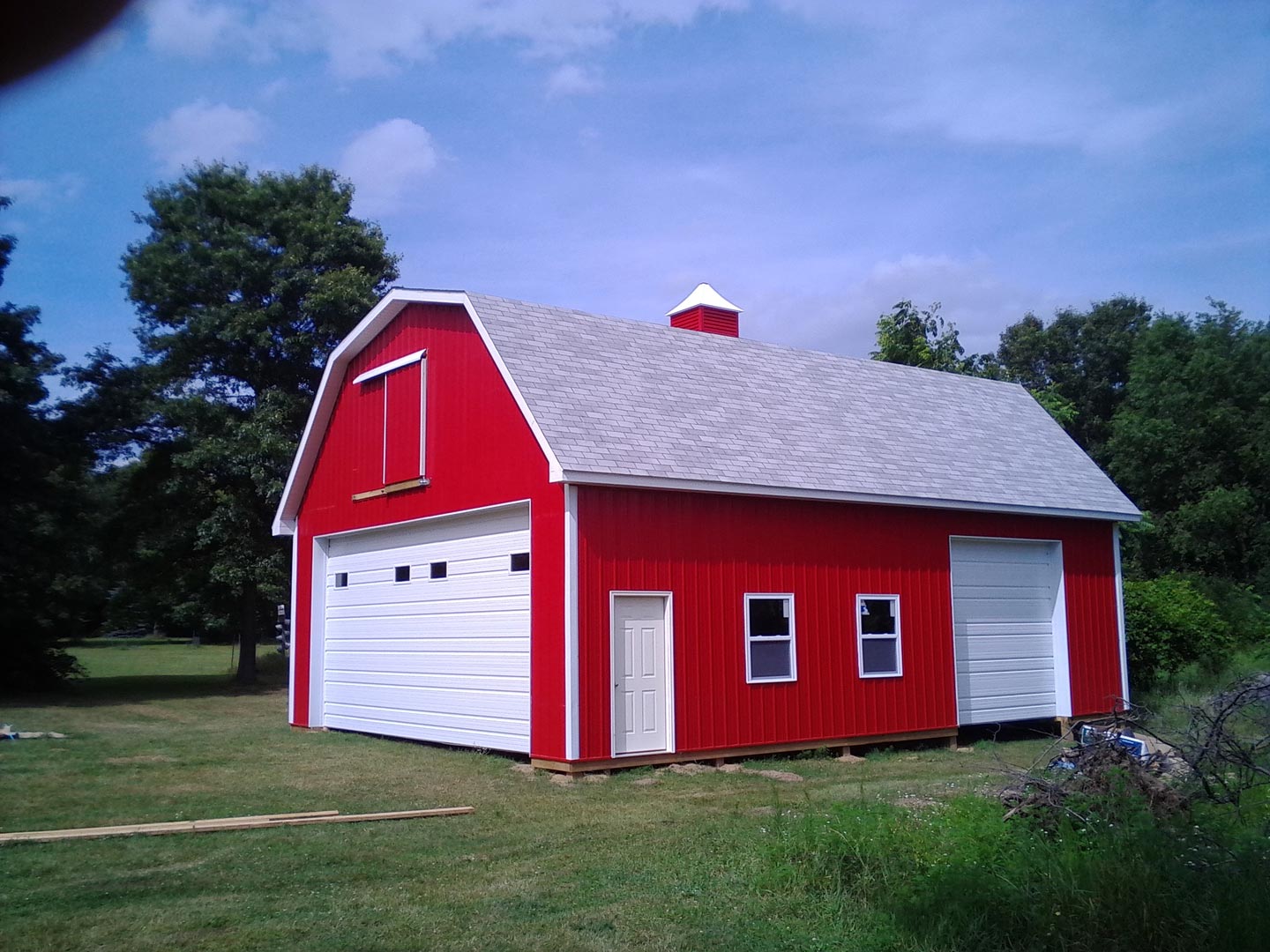 Red barn with white doors and trim, gray roof, on a grassy lot under a blue sky.