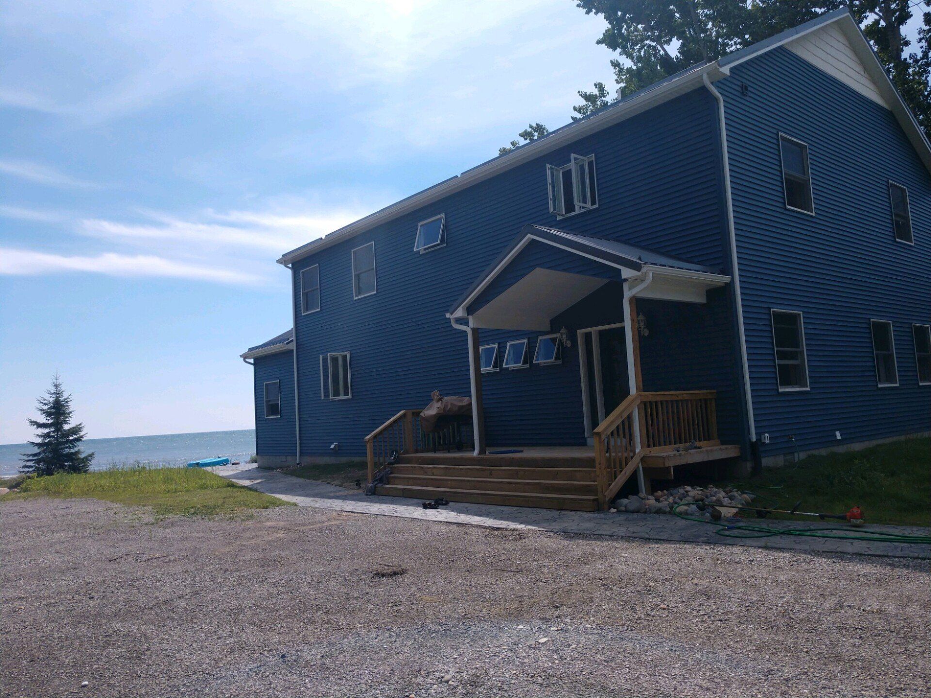 Blue house with porch and lake view on a gravel driveway under a partly cloudy sky.
