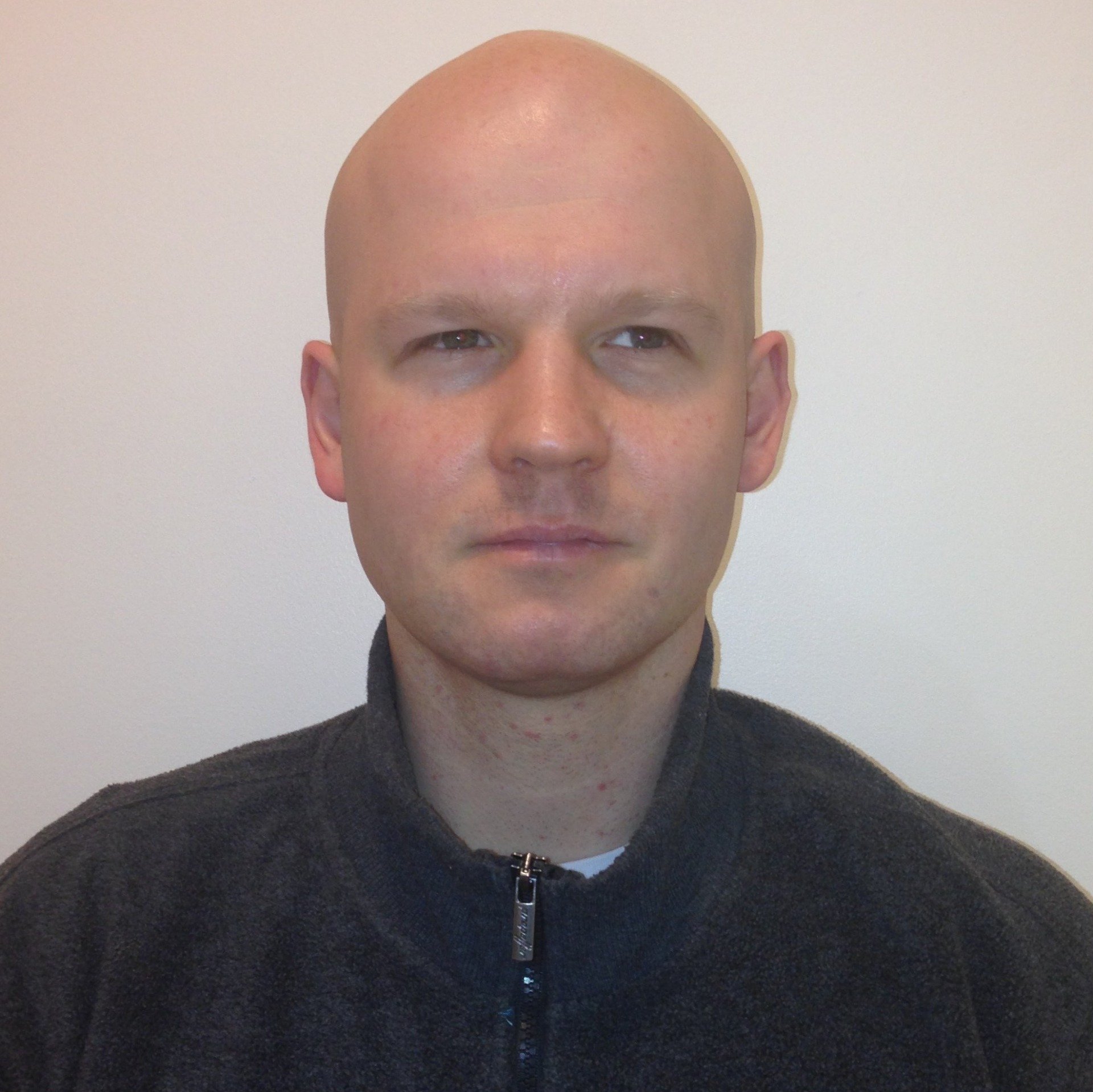 A bald man wearing a black jacket looks at the camera