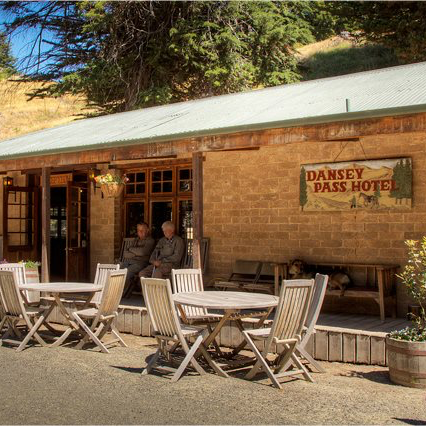 Stone Dansey Pass Hotel building with outdoor wooden tables and chairs, with people sitting on a porch.