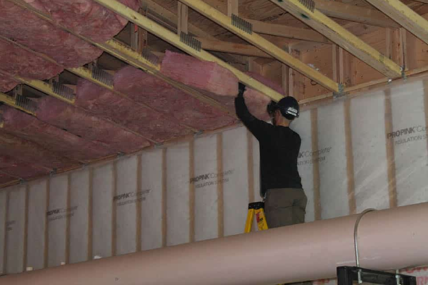 A man is standing on a ladder holding a piece of insulation.