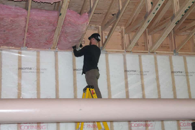 A man is standing on a ladder working on a ceiling