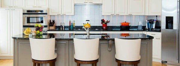 A kitchen with three bar stools and a stainless steel refrigerator
