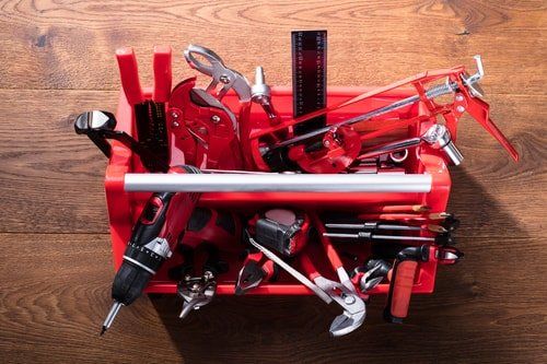 red handyman tool box with a variety of different tools in a black and red colorway sitting on wooden desk.