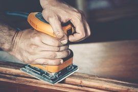 typical handyman carpenter sanding down a piece of furniture that was done from wood oak. sanding machine sanding down wood frame with a smooth round edge.