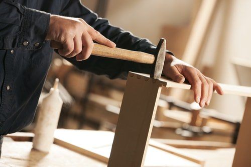 handyman carpenter putting together a wooden project hitting the side of the wood with a metal hammer.