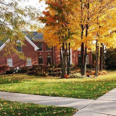 Brick house with golden autumn trees and green lawn.