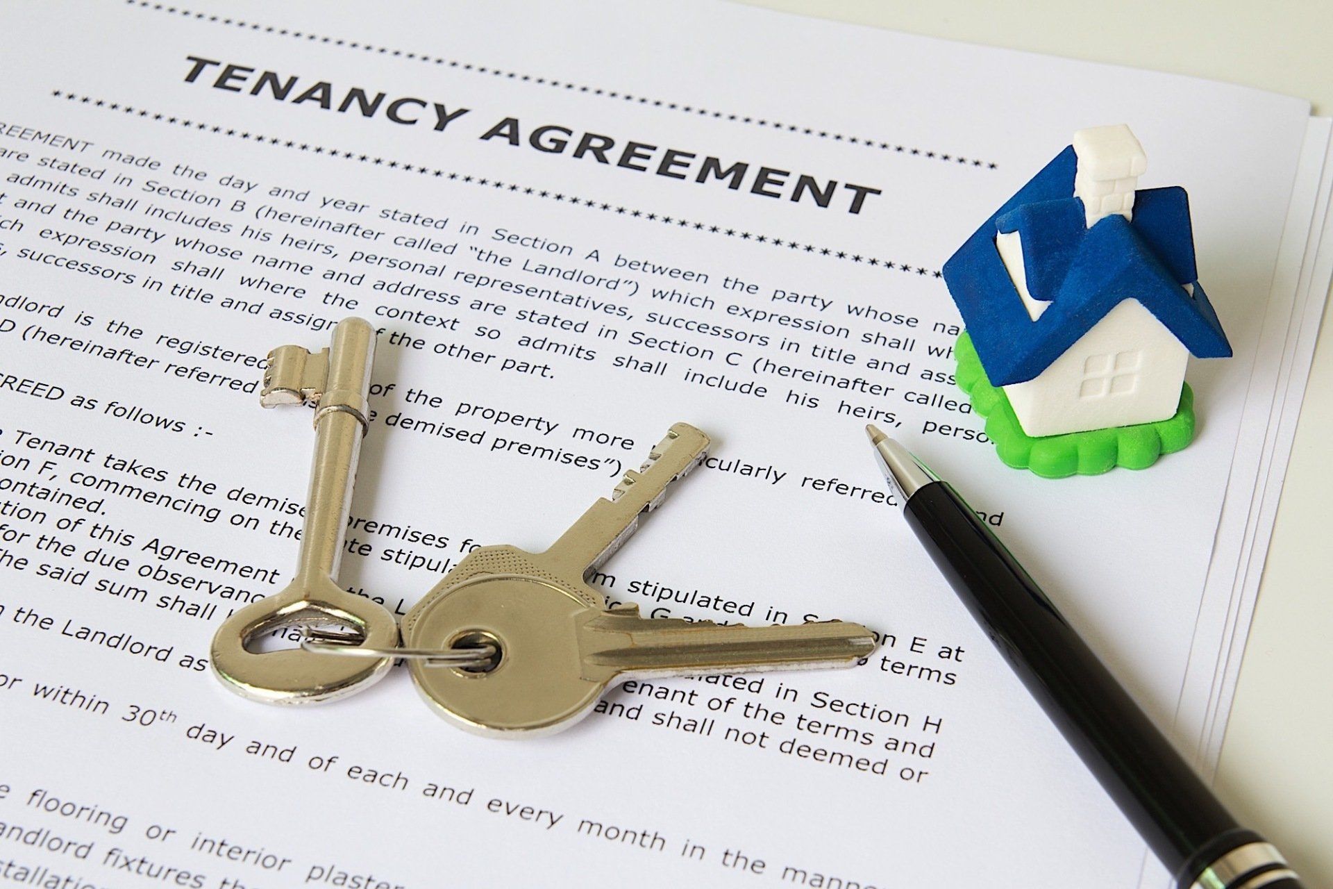Tenancy agreement with keys, pen, and small house figurine.