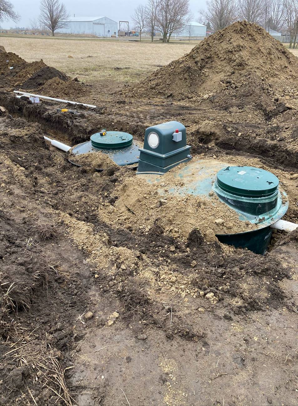 Septic system installation in progress. Tanks, pipes, and dirt mound in an open field setting.