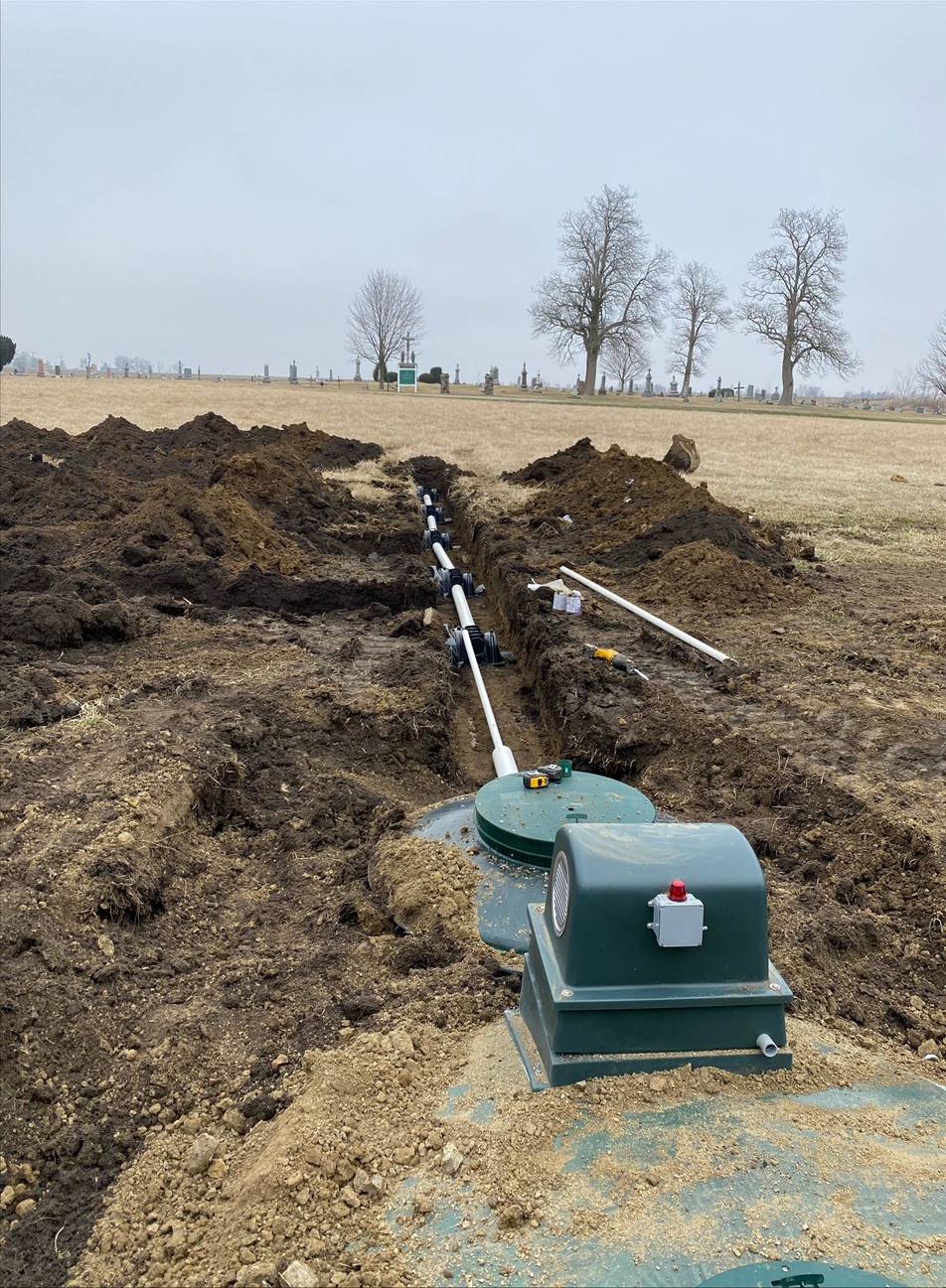 Installation of a septic system: green tanks and buried pipes in an open field with trees in the background.