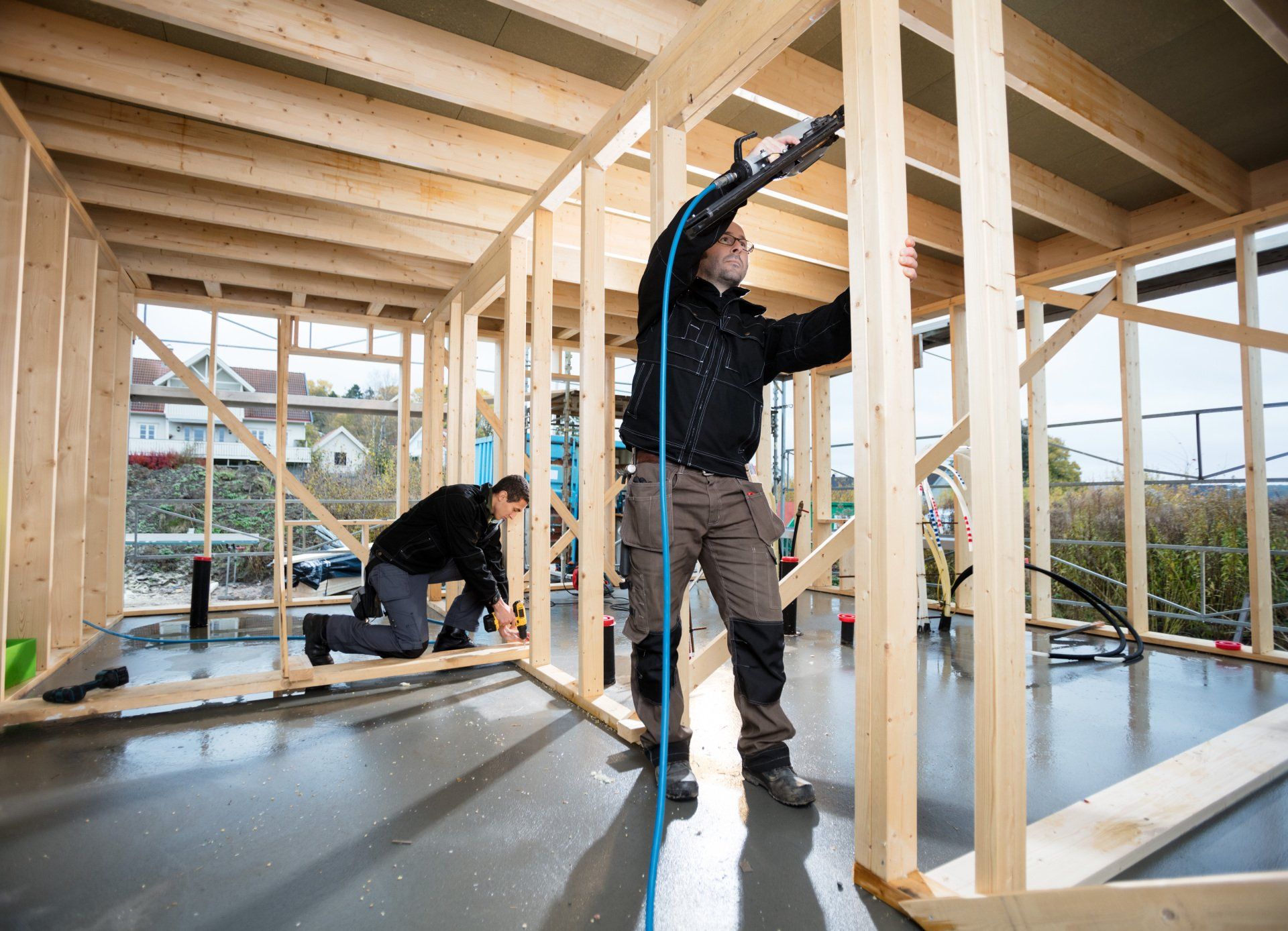 Two men are working on a wooden frame of a house.