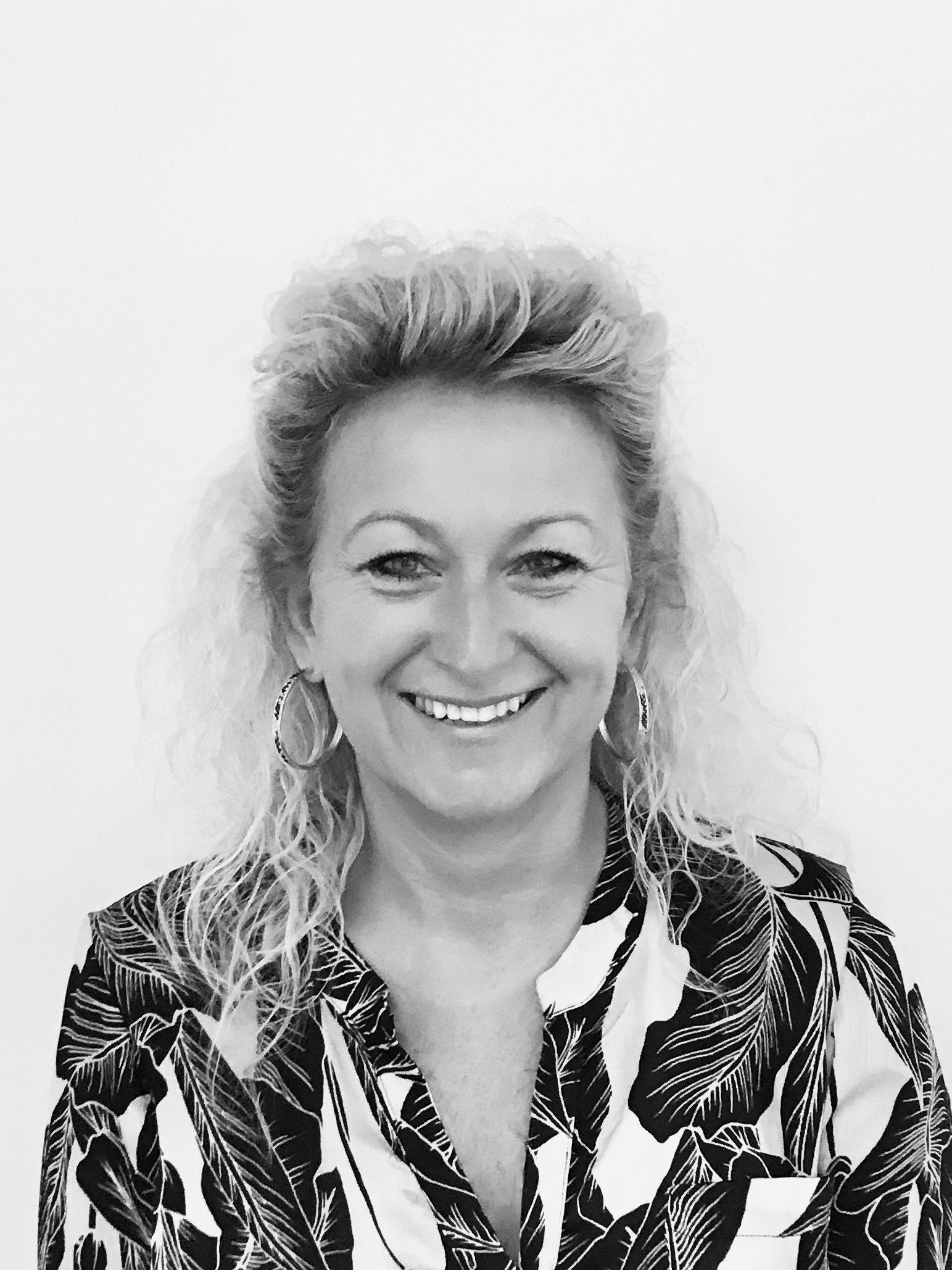 A smiling person with curly hair, wearing large hoop earrings and a patterned top, set against a plain background.