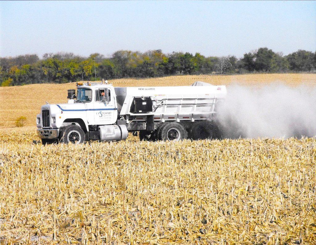 Truck spreading fertilizer on a harvested cornfield, creating a dust cloud.