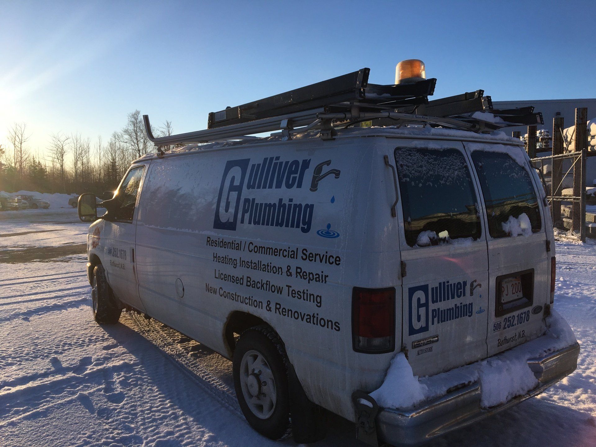 White Gulliver Plumbing van in snow with a ladder rack and an emergency light.