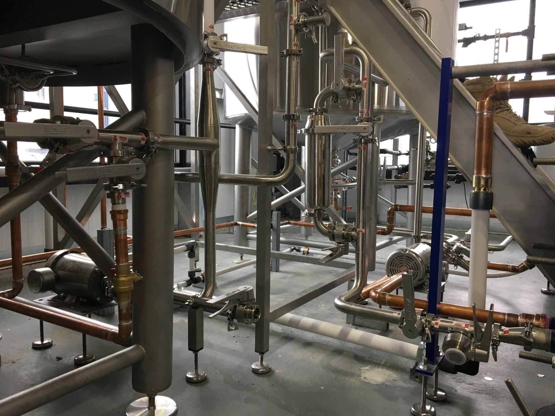 Industrial brewery equipment with stainless steel pipes and copper fittings.
