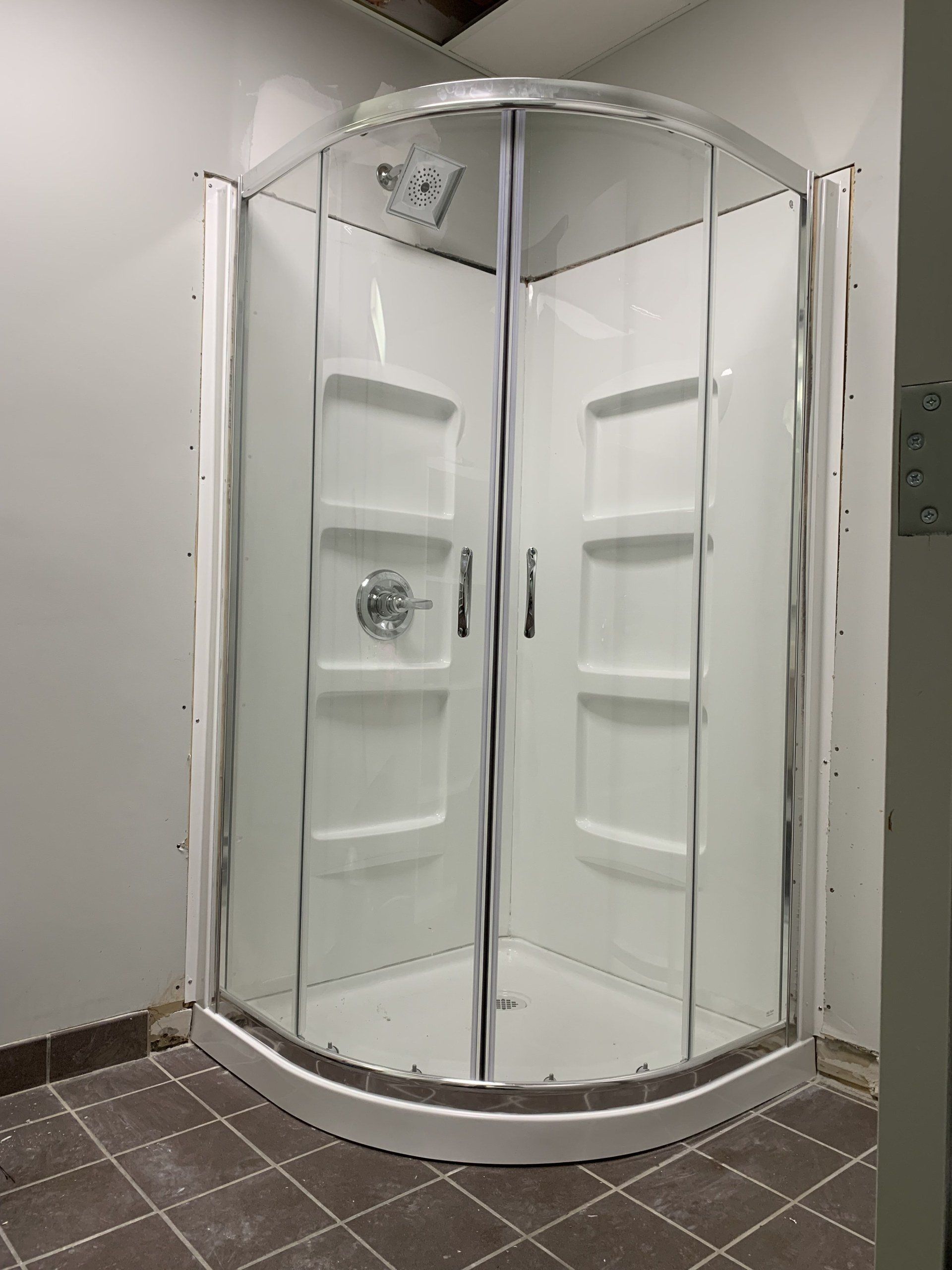White, enclosed corner shower with glass doors, silver trim, and built-in shelves.