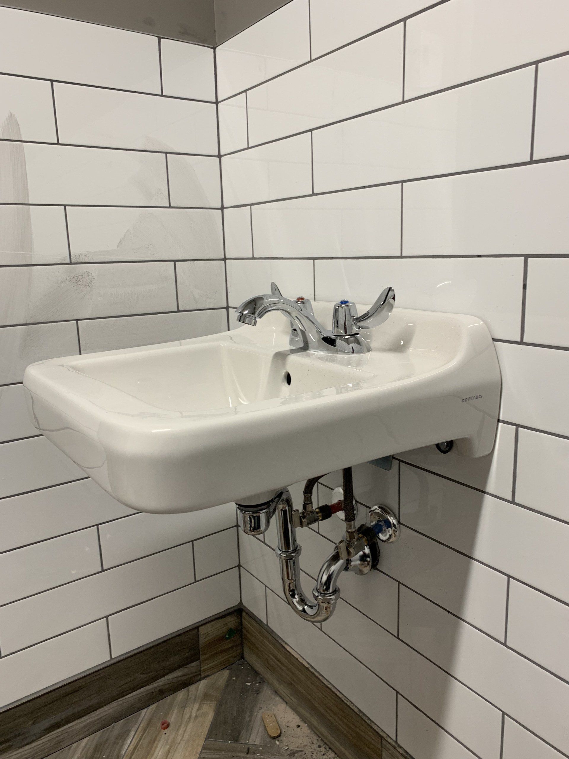 White wall-mounted sink with chrome fixtures, set against a subway-tiled wall.