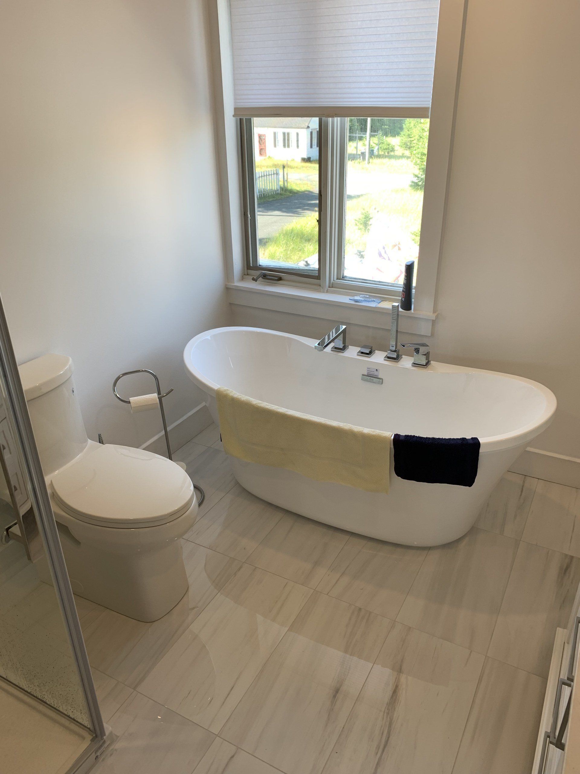 Bathroom with a white oval bathtub by a window and a toilet on the left.