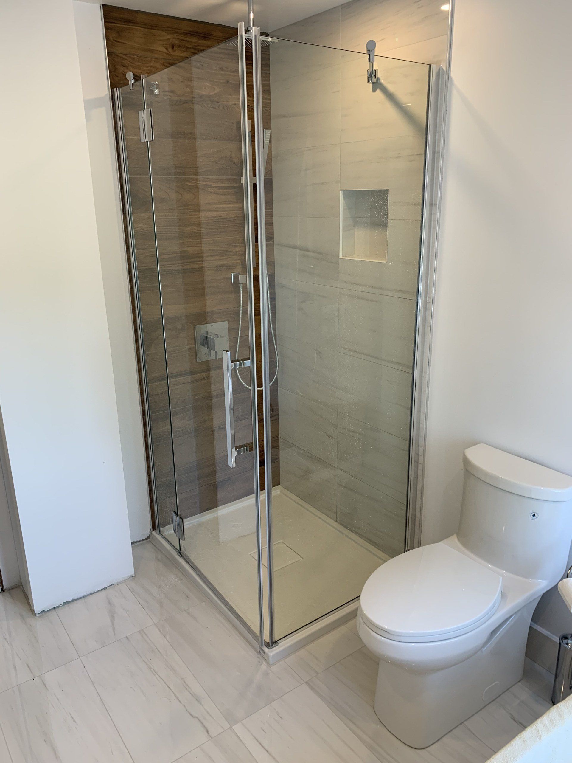 Modern bathroom with a glass shower, toilet, and light-colored tile walls.